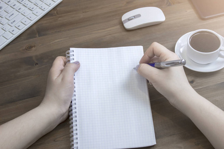 s hand writing in empty notepad placed on  desktop keyboar