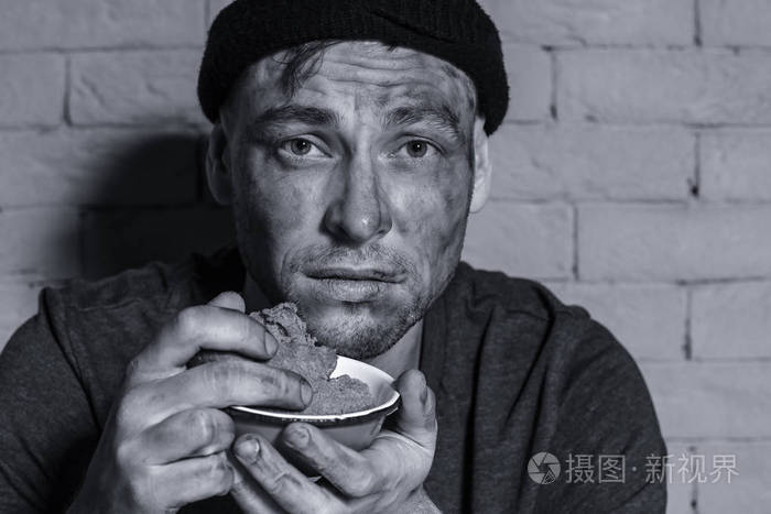 饥肠辘辘的穷人拿着一碗面包贴在砖墙上