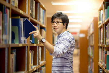 亚洲年轻男子大学学生在图书馆选书