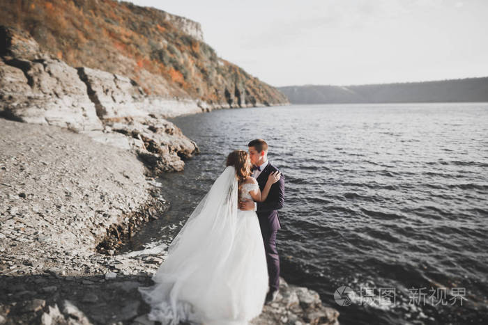 婚礼情侣接吻和拥抱蓝色海边的岩石上