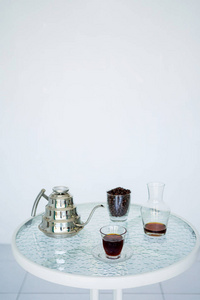 在透明的玻璃和金属水壶中供应咖啡，里面有咖啡豆和一个壶，有很好的咖啡气味。 背景模糊，全是白色的。 侧视图与复制空间