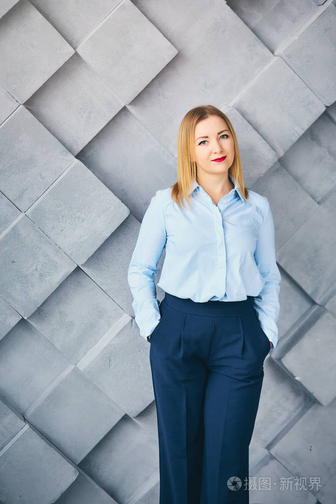 一个年轻的笑容迷人的女人在办公室的衣服上灰色的墙壁背景的肖像.