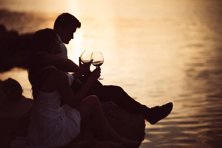 浪漫的一对夫妇在日落时分在码头上喝酒，seaside.romance.two人们在海边度过了一个浪漫的夜晚，喝着一杯葡萄酒。享受