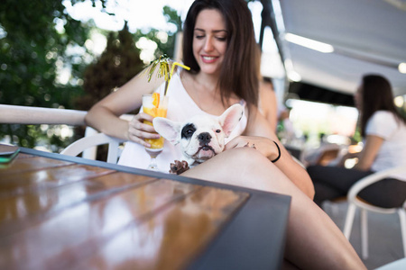 漂亮的年轻女人和她可爱的法国斗牛犬小狗坐在咖啡馆里。 以狗为主题的人图片