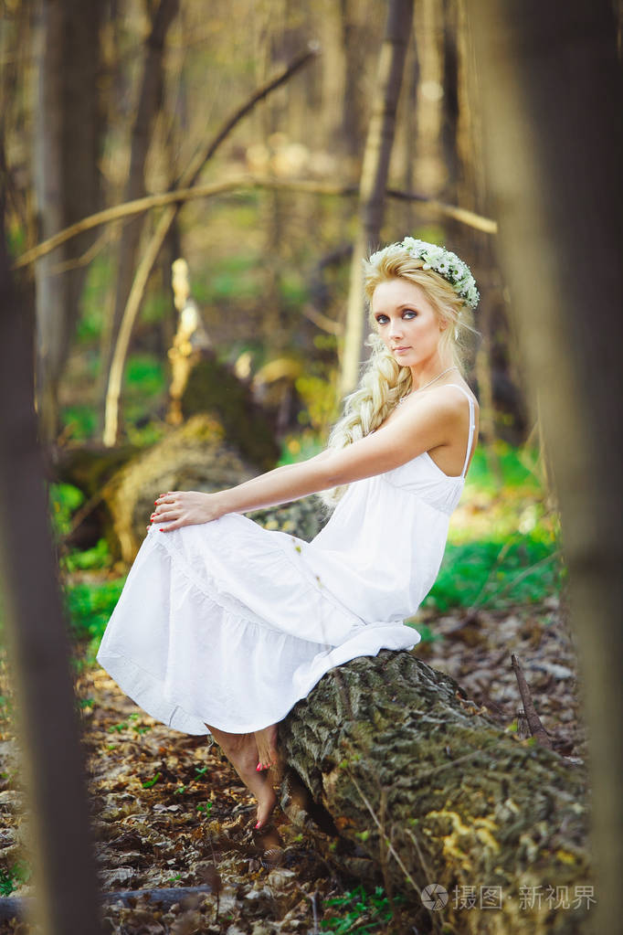 美丽的妇女穿着白色礼服坐在树绿色森林
