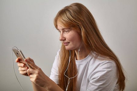 年轻的红发女人，带着雀斑，一边拿着电话，一边用耳机接视频电话