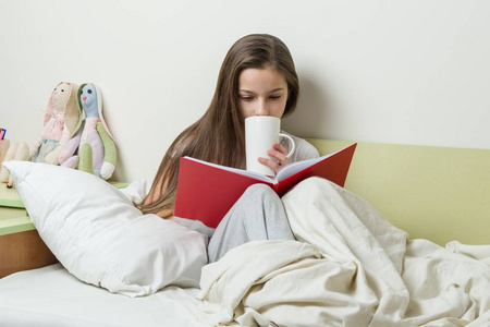 10岁的女孩在睡衣读书和举行杯子茶