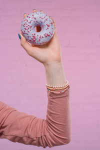 一个女人手拿着美味的釉面甜甜圈，手拿着粉红色的砖墙