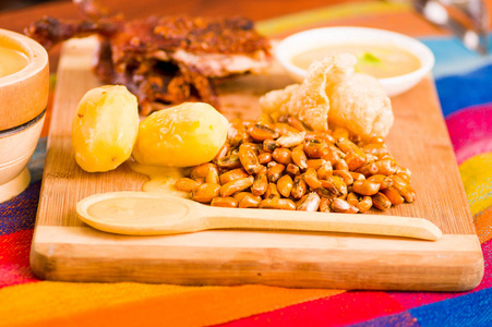 切件煮熟的 guine 猪肉躺在木表面旁边的土豆, tostados 和碗萨尔萨