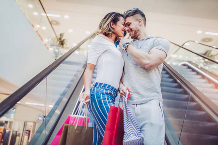 快乐的年轻夫妇带着购物袋，用电梯在商场里
