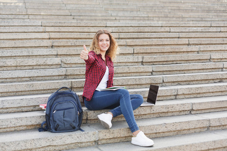 微笑的女学生坐在楼梯上使用笔记本电脑户外