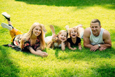 度假休闲活动生活方式理念。 母亲和父亲日。 孩子们和父母躺在绿草上。 幸福的童年家庭爱情。 女孩女人和男人在夏天的风景上微笑。