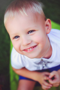 快乐的蓝眼睛金发男孩看着相机微笑着。柔和的暖色调