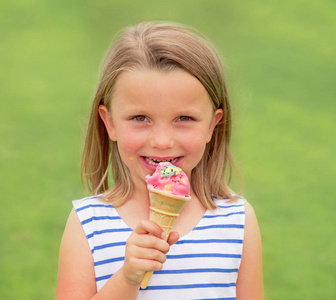可爱和美丽的金发女孩的肖像6或7岁吃美味的冰淇淋微笑着快乐的绿色草地上孤立