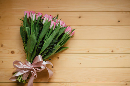 粉红色的郁金香和香水的花束在木质背景上的美丽的弓