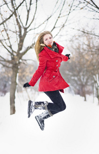 漂亮的金发女孩，戴着手套，穿着红色外套，戴着红色帽子，在冬雪中摆姿势。冬日美景中的美女。年轻女子