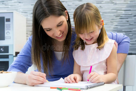 母亲和孩子用蜡笔画画，坐在厨房的桌子旁