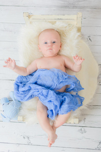 婴儿躺在一张小婴儿床上，用蓝色柔软的材料包裹着