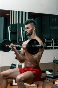 健身房里的男子用杠铃表演二头肌卷发