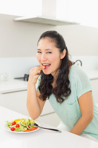 一位年轻女子在厨房吃沙拉的画像