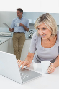 女人用笔记本电脑男人在厨房看报纸
