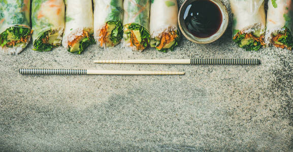 海莉亚洲美食。 平躺的纯素春饭纸卷与蔬菜，酱油，筷子，在混凝土背景上，俯视复制空间宽的构图。 吃素食