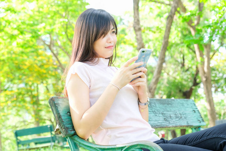微笑的女人在公共公园坐在长凳上放松使用手机