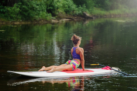 年轻的运动妇女在一个湖上的桨板上做健身