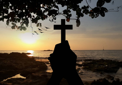 崇拜日落剪影的人手拿着十字架,神圣,祈祷上帝的祝福,模糊了日落的