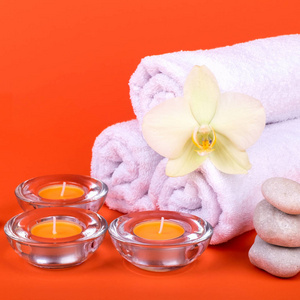 在橙色背景下享受水疗放松的毛巾蜡烛和兰花花