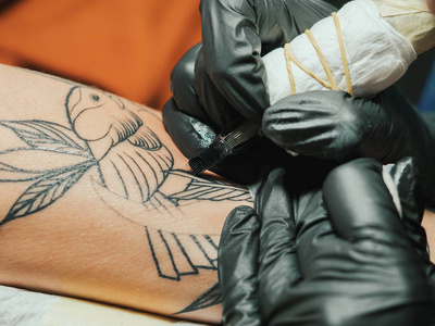 纹身艺术家在工作。妇女在黑色乳胶手套纹身一个年轻的男子手与彩色图片在演播室。宏