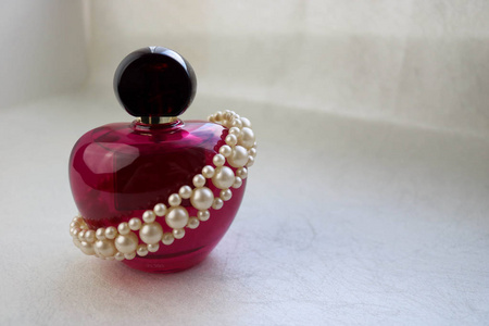 粉红色美丽的玻璃透明瓶女性香水装饰白色珍贵珍珠，并放置一个简单的文字在一个浅白色的背景。