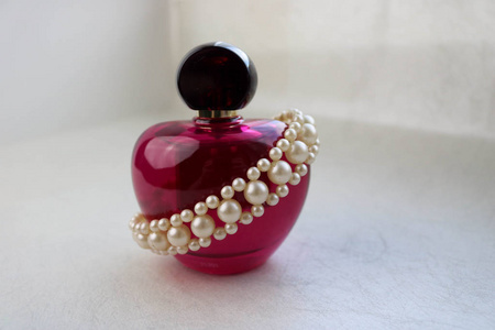 粉红色美丽的玻璃透明瓶女性香水装饰白色珍贵珍珠，并放置一个简单的文字在一个浅白色的背景。