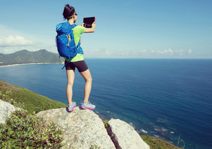 女子背包客使用数码平板电脑海边山崖边缘