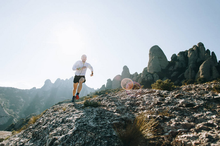 穿短裤风衣的男子在山径上沿岩石或悬崖奔跑，参加马拉松式的马拉松赛跑，或在阳光明媚风景优美的天气进行训练