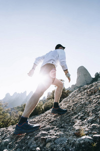 职业运动员跑步者在比赛或锻炼中爬上陡峭的岩石或悬崖。 穿着短跑短裤进行马拉松训练。 健康生活方式选择