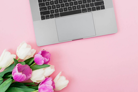 粉红色背景上的笔记本电脑和郁金香花。 平躺着。 上面的风景。 带有复制空间的构图。
