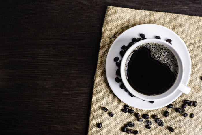 白色杯子里的黑咖啡和木桌背景上的咖啡豆
