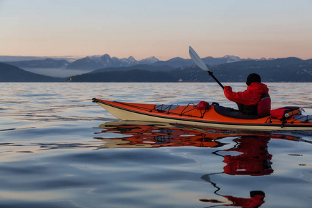 在一个充满活力和丰富多彩的冬季日落期间，海上皮艇上的冒险人正在皮划艇。 摄于加拿大不列颠哥伦比亚省温哥华。 冒险度假概念