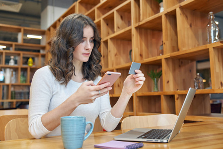 现代年轻女子女孩坐在一张桌子在咖啡馆与手提电脑智能手机支付在线订单