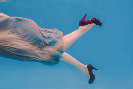 s legs in violet shoes underwater in the swimming pool