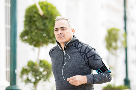 健康的中年人在城市里跑步，用智能手机听音乐