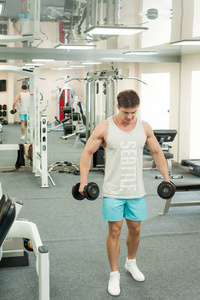 年轻的男性健美运动员在健身房训练，使用运动设备和健身设备来改善身体的健康和美丽。
