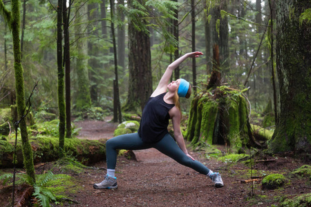 年轻的白种人女孩正在雨林里练习瑜伽。 在加拿大温哥华北部的Capilano峡谷拍摄。