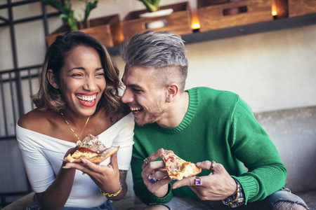 混合种族夫妇在现代咖啡馆里笑着吃比萨饼