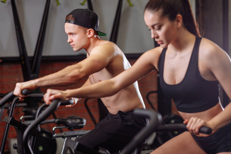 妇女和男子骑自行车在健身房, 锻炼腿做有氧运动自行车自行车