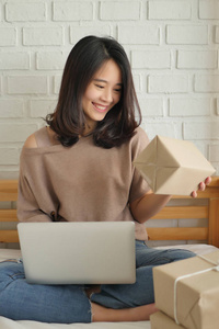 快乐的女人与电脑和产品包盒在家里, 工作在家里的商品交付概念