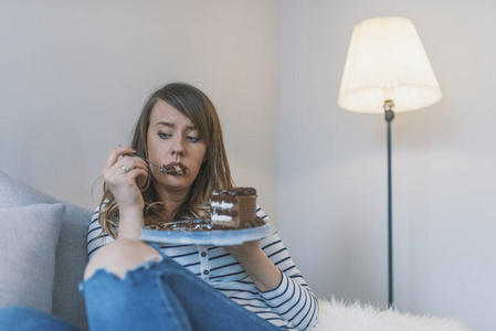 沮丧的女人吃蛋糕。伤心不开心的女人吃蛋糕。伤心的女人吃甜蛋糕。接近女人吃巧克力蛋糕。食品，垃圾食品，烹饪，烘焙和假日概念
