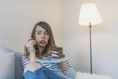 沮丧的女人吃蛋糕。伤心不开心的女人吃蛋糕。伤心的女人吃甜蛋糕。接近女人吃巧克力蛋糕。食品，垃圾食品，烹饪，烘焙和假日概念