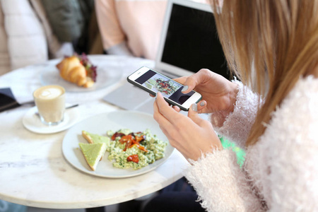 年轻女子在咖啡馆的餐桌上用手机拍照美味的食物